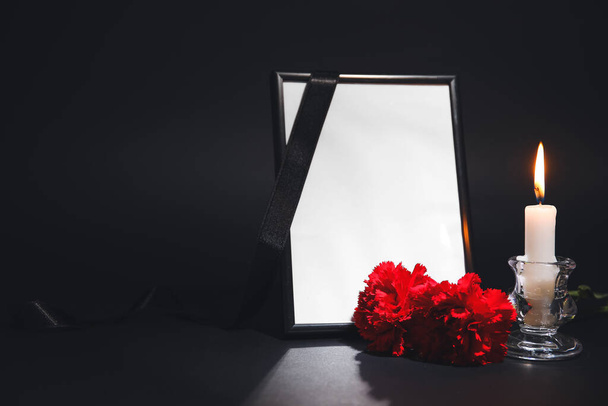 Photo frame with carnation flowers and candle on dark background - Фото, изображение