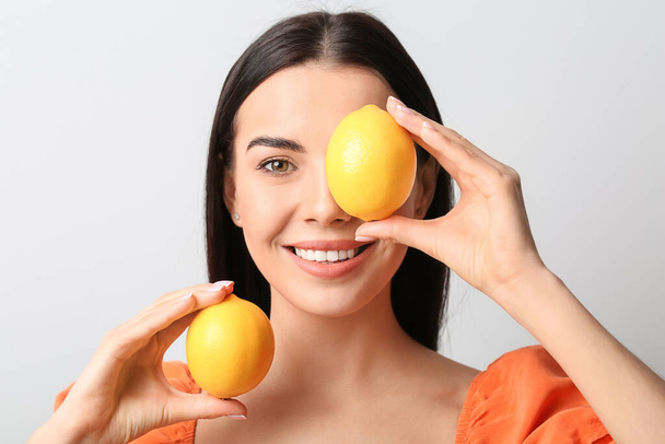 Beautiful young woman with lemons on light background - 写真・画像