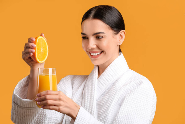 Hermosa mujer joven haciendo jugo de naranja fresco en el fondo de color - Foto, imagen