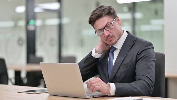 Müder Geschäftsmann mittleren Alters mit Laptop hat Nackenschmerzen im Büro  - Foto, Bild