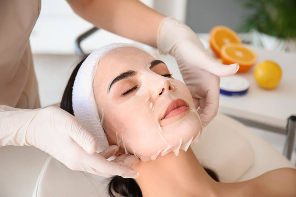 Cosmetologue appliquer masque feuille sur le visage de la femme dans le salon de beauté - Photo, image