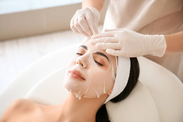 Cosmetologist aplicando máscara de folha no rosto da mulher no salão de beleza - Foto, Imagem