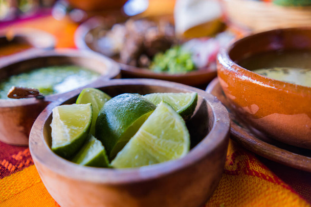 Bowls of lime slices, green sauce, and lamb broth on colorful tablecloth - Photo, Image