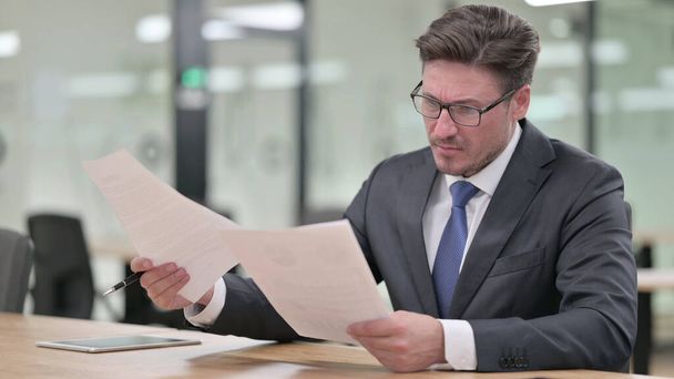 Серйозний середнього віку бізнесмен робить папери в офісі
  - Фото, зображення