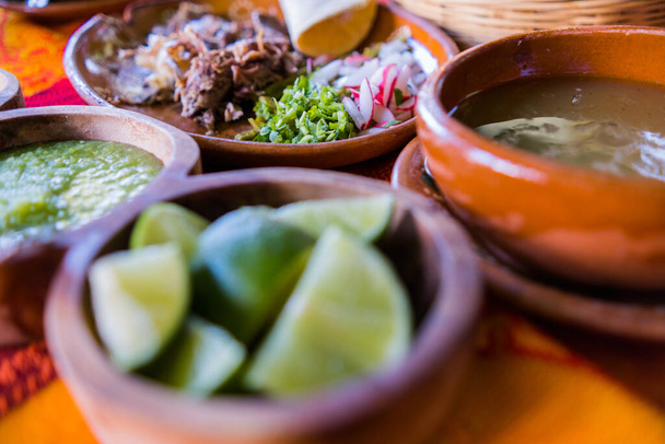 Bowls of lime slices, green sauce, and lamb broth on colorful tablecloth - Photo, Image