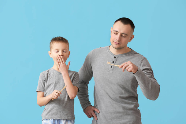 Schläfriger Vater und kleiner Sohn beim Zähneputzen auf farbigem Hintergrund - Foto, Bild