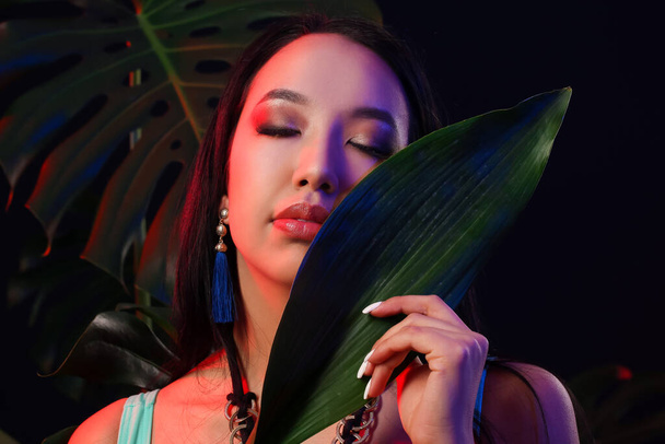 Belle femme asiatique avec feuille tropicale sur fond sombre - Photo, image
