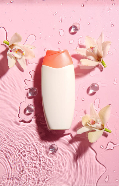 Bottle of cosmetic product and flowers in water on color background - Photo, Image
