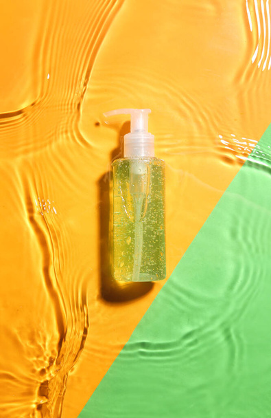 Bottle of cosmetic product in water on color background - Photo, Image