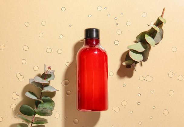 Пляшка косметичного продукту та гілок евкаліпта на кольоровому фоні з краплями води
 - Фото, зображення