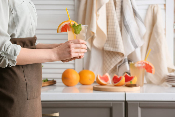 Woman with glass of tasty grapefruit lemonade in kitchen - Foto, imagen