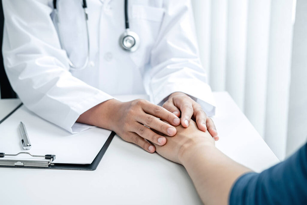 Doctor holding hands on patient about bad news at consulting room, to encourage, to supporting,  to fight for disease and to advice treatment and medicine at his hospital office - Photo, Image