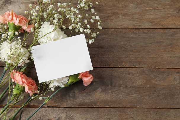 Свежие гвоздичные цветы с пустым листом бумаги на деревянном фоне - Фото, изображение