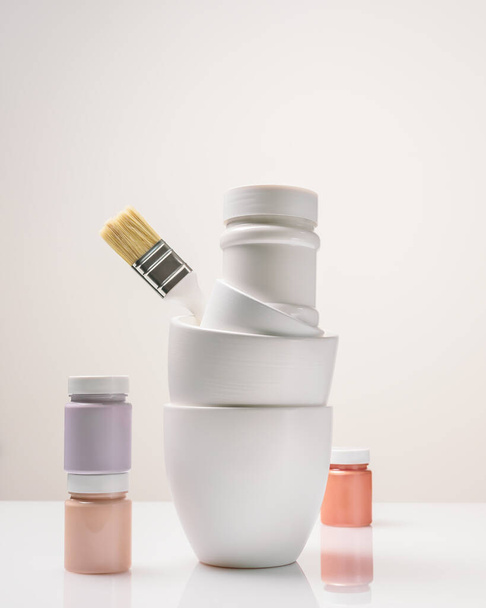 Vertical composition with paint cans, jars and a brush on a light background with copy space. Mockup for paints, lacquers. Artist's workplace, preparation for decorative, creative and artistic works - Foto, Imagen