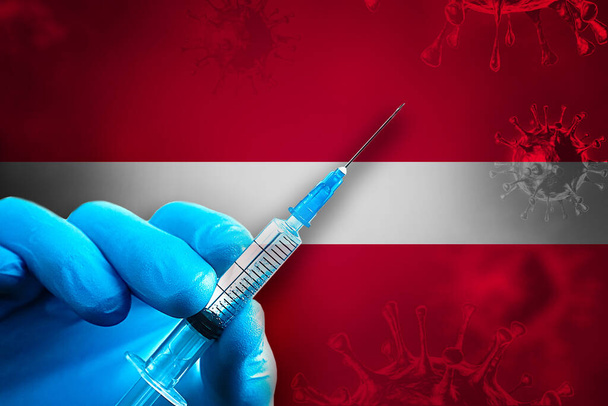 Lettonia Campagna di vaccinazione Covid-19. Una mano in un guanto di gomma blu tiene una siringa con vaccino antivirale covid-19 davanti alla bandiera lettone. Concetto di vaccinazione contro il coronavirus - Foto, immagini