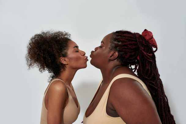 Side view of slim and plus size african american women in underwear making kiss gesture to each other, posing together isolated over gray background - Φωτογραφία, εικόνα