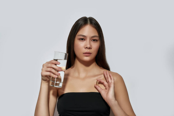 Young asian woman holding pill and glass of water - Fotografie, Obrázek