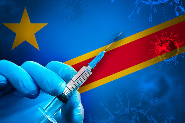 Congo DR Covid-19 Campagna di vaccinazione. Una mano in un guanto di gomma blu tiene una siringa con vaccino antivirale covid-19 davanti alla bandiera CongoDR. Concetto di vaccinazione contro il coronavirus - Foto, immagini