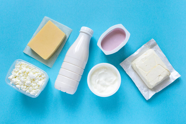 Flat lay of dairy products. Milk, curd, sour cream, cheese and butter on blue background, top view. - Photo, image