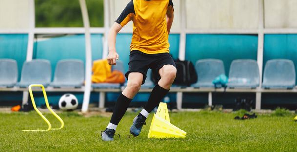 Юный футболист, бегущий на тренировочном поле. Мальчик занимается футболом с помощью спортивного инвентаря. Мальчик захватывает дриблинг и ловкость навыков - Фото, изображение