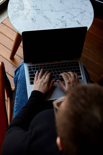 Egy fiatal lány szemüveggel, rövid hajjal és orrpiercinggel ül egy kávézóban és egy laptopon dolgozik. A szabadúszó és távoli munkavégzés vagy képzés fogalma. - Fotó, kép