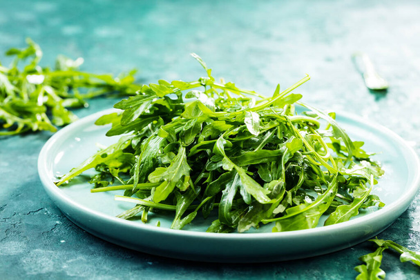 close-up view of fresh arugula leaves on plate on rustic background - Fotografie, Obrázek