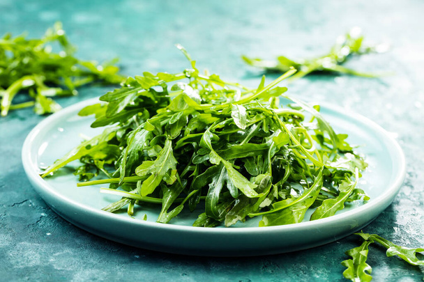 close-up view of fresh arugula leaves on plate on rustic background - Foto, Bild