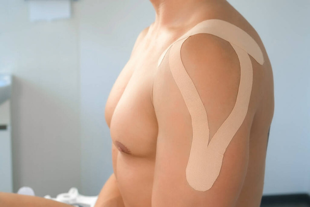 Kinesiology tapes on mans shoulder and hand for fixation of muscles, closeup. - Фото, зображення
