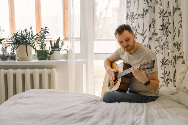 男は自宅の部屋でアコースティックギターを演奏する。趣味はミュージシャン。家での生活 - 写真・画像