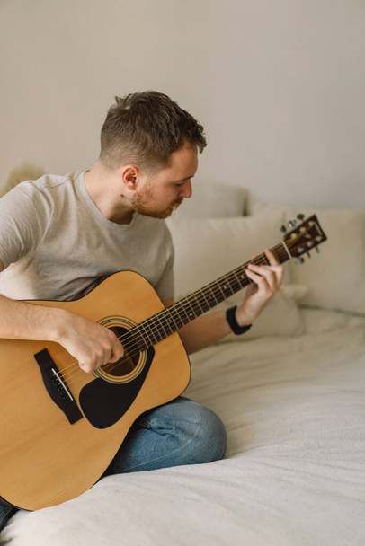 Man plays an acoustic guitar in a room at home. Hobby a musician. - Fotó, kép