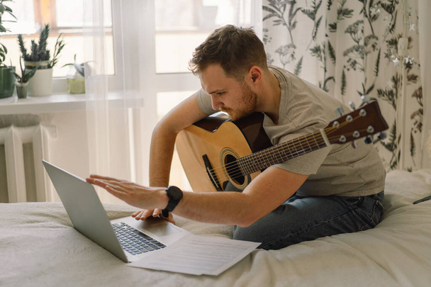 Ο άνθρωπος παίζει ακουστική κιθάρα σε ένα διαδικτυακό μάθημα. Hobby ένας μουσικός. - Φωτογραφία, εικόνα