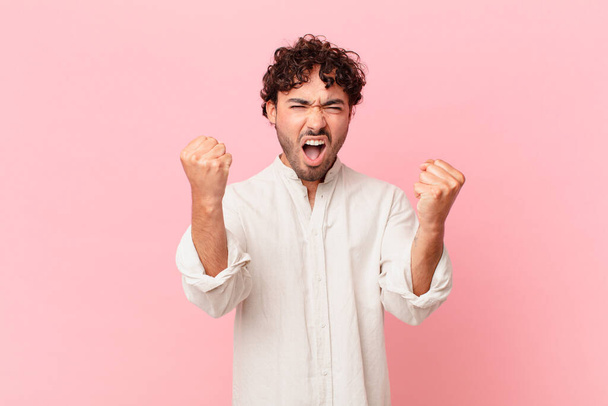 hispanic handsome man shouting aggressively with an angry expression or with fists clenched celebrating success - Fotografie, Obrázek