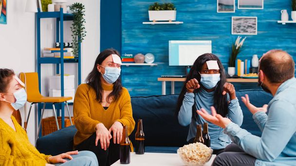 Multiracial colleagues with protective masks playing game with sticky notes - Photo, Image
