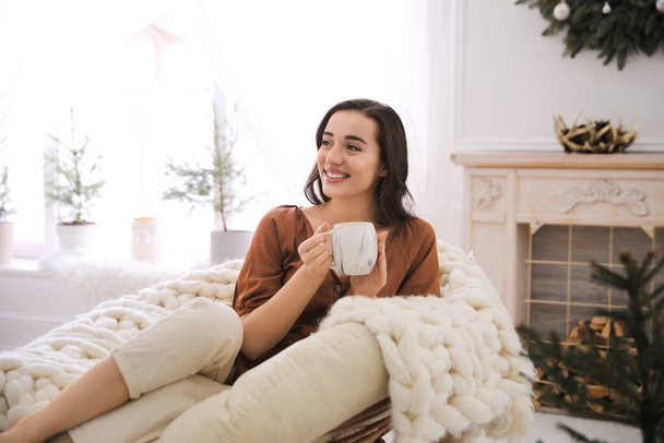 Woman with hot drink resting in comfortable papasan chair at home - Fotoğraf, Görsel