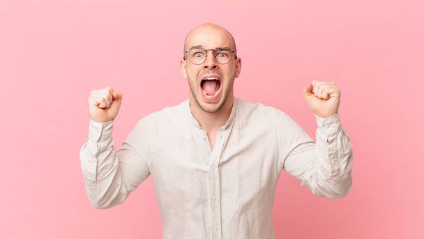 bald man shouting aggressively with an angry expression or with fists clenched celebrating success - Foto, Imagen