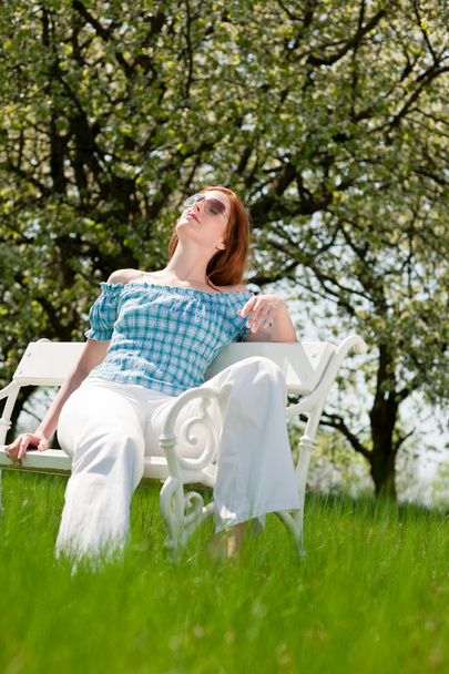 Рыжая женщина с весенним солнцем на белой скамейке на лугу; мелкий DOF
 - Фото, изображение
