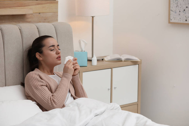 Sick young woman with napkins and nasal spray in bed at home - Foto, Imagen