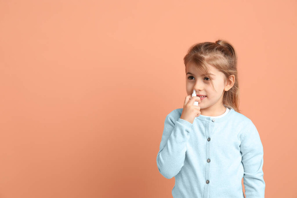Sick little girl using nasal spray on coral background. Space for text - Фото, изображение