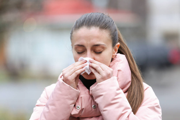 Ill woman with paper tissue sneezing outdoors - Foto, Imagem