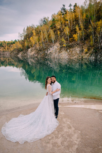Newlyweds are standing near a beautiful lake. - Фото, зображення