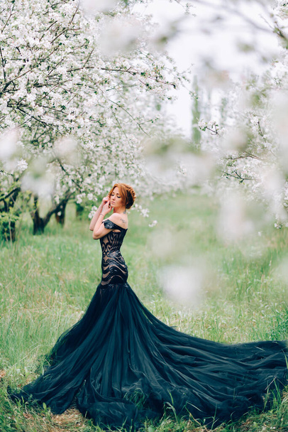 A young woman in a black dress is standing in a blooming garden. - Foto, Bild