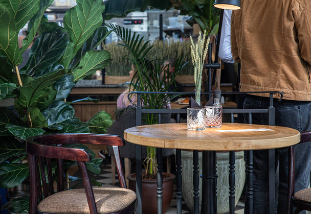 Details of the interior of modern cafe or coffee house with tropical plants, wooden tables, chairs and wheat ears in glass vase. Modern design concept. - 写真・画像