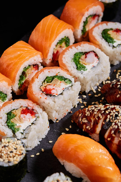 Japanse Oosterse keuken. Close-up van gesneden Philadelphia sushi op een zwart bord op een donkere achtergrond. Selectieve focus, wazige achtergrond. Japans restaurant menu. - Foto, afbeelding
