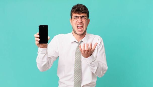 business with a smartphone looking desperate and frustrated, stressed, unhappy and annoyed, shouting and screaming - Photo, Image