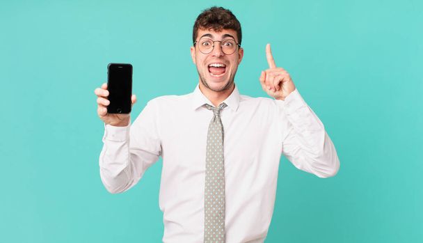 business with a smartphone feeling like a happy and excited genius after realizing an idea, cheerfully raising finger, eureka! - Фото, изображение