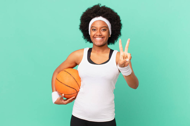 afro donna sorridente e guardando felice, spensierata e positiva, gesticolando la vittoria o la pace con una mano. concetto di basket - Foto, immagini