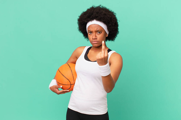 afro woman feeling angry, annoyed, rebellious and aggressive, flipping the middle finger, fighting back. basketball concept - Foto, afbeelding