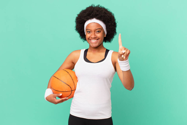 afro woman smiling and looking friendly, showing number one or first with hand forward, counting down. basketball concept - Foto, immagini