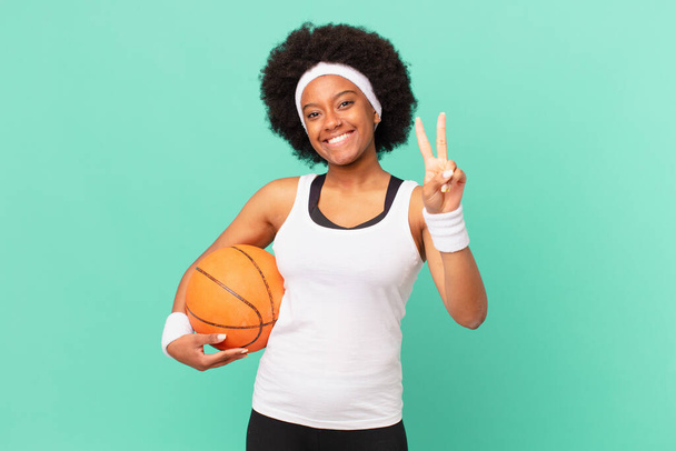 afro woman smiling and looking friendly, showing number two or second with hand forward, counting down. basketball concept - Foto, imagen