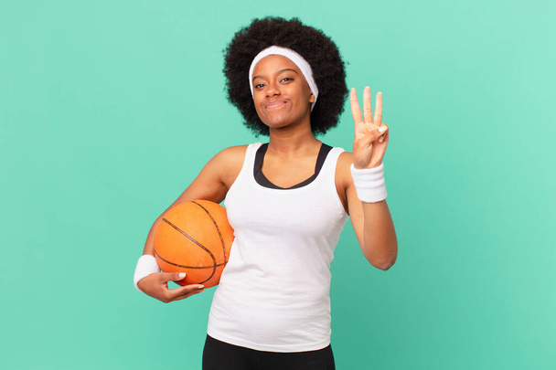 afro woman smiling and looking friendly, showing number three or third with hand forward, counting down. basketball concept - Foto, Imagem